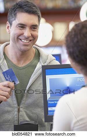Stock Image - Hispanic man holding up credit card at check out. Fotosearch