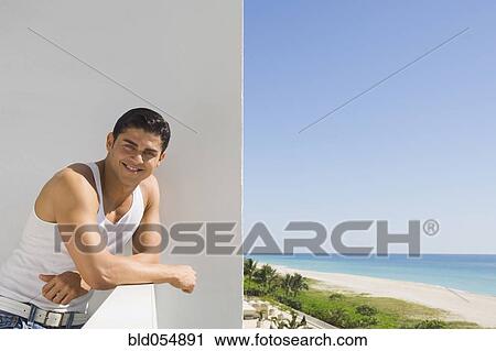 Stock Image - Hispanic man leaning on balcony railing. Fotosearch