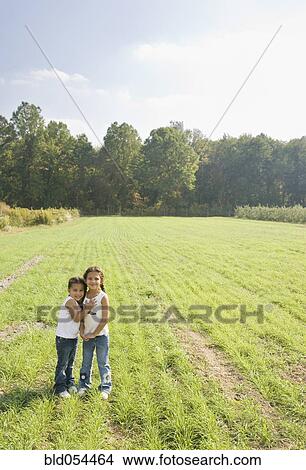 Picture - Hispanic sisters hugging in field. Fotosearch
