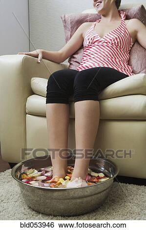 Stock Photograph - Hispanic woman soaking feet in water with flower petals. Fotosearch