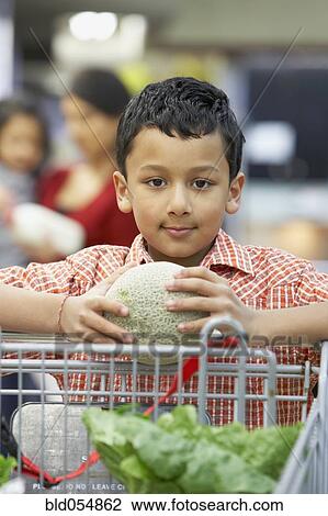 Stock Image - Indian boy holding fruit at grocery store. Fotosearch