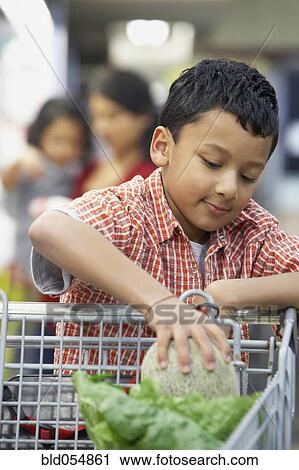 Stock Image - Indian boy putting fruit in shopping cart. Fotosearch