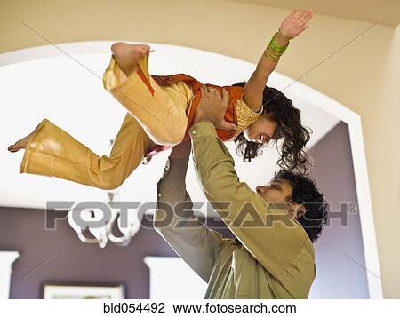 Stock Image - Indian father holding daughter in air. Fotosearch