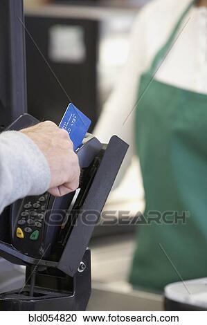 Stock Image - Man swiping credit card at grocery store checkout. Fotosearch