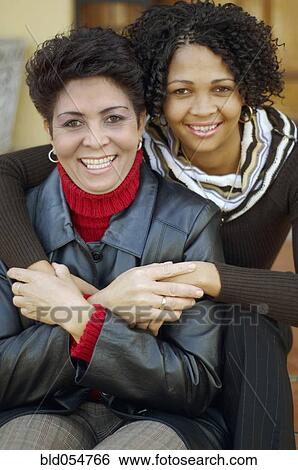 Stock Photograph - Mixed Race mother and adult daughter hugging. Fotosearch