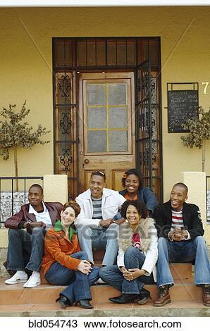 Stock Image - Multi-ethnic friends sitting on porch steps. Fotosearch