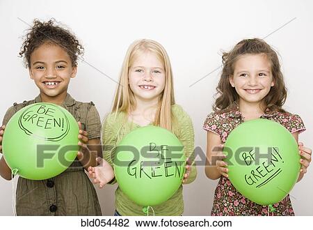 Stock Image - Multi-ethnic girls holding green balloons. Fotosearch