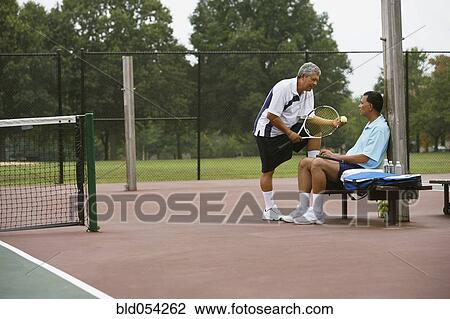 Stock Image - Multi-ethnic men talking on tennis court. Fotosearch