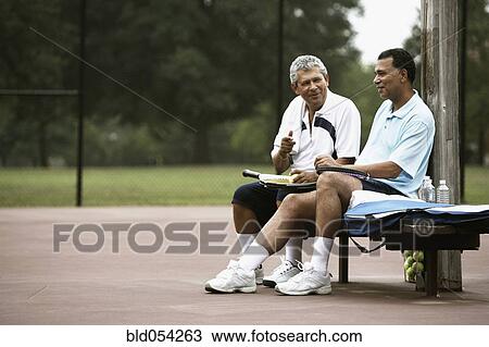 Stock Image - Multi-ethnic men talking on tennis court. Fotosearch