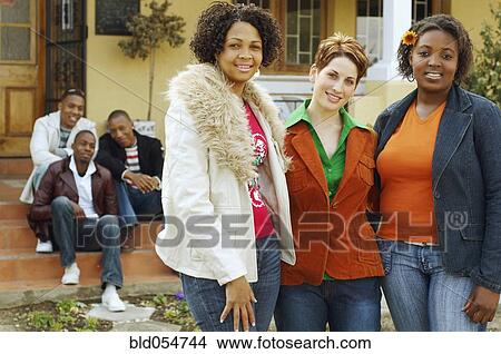 Picture - Multi-ethnic women hugging with friends in background. Fotosearch