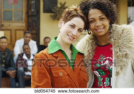 Stock Photography - Multi-ethnic women hugging with friends in background. Fotosearch