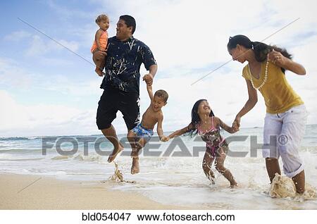 Stock Photo - Pacific Islander family jumping in ocean surf. Fotosearch