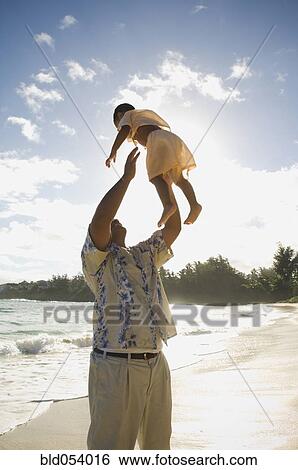 Stock Photograph - Pacific Islander father playing with son at beach. Fotosearch