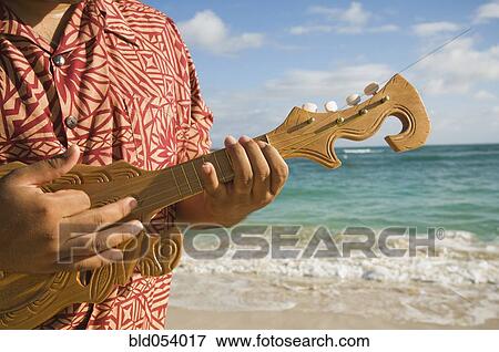 Stock Photo - Pacific Islander man playing instrument at beach. Fotosearch