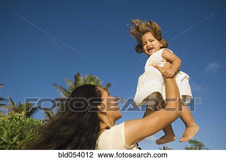 Stock Image - Pacific Islander mother holding daughter in air. Fotosearch