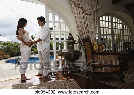 Stock Image - Pregnant Hispanic couple standing in doorway. Fotosearch