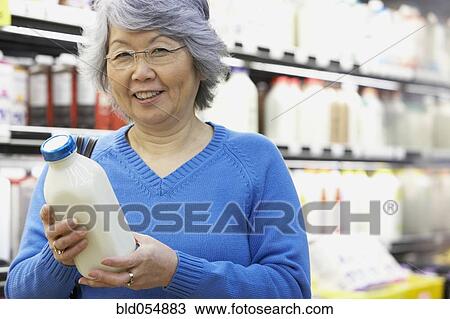Stock Image - Senior Asian woman holding milk in grocery store. Fotosearch