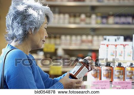 Stock Photo - Senior Asian woman reading vitamin label. Fotosearch