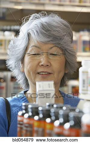 Stock Photo - Senior Asian woman reading vitamin label. Fotosearch