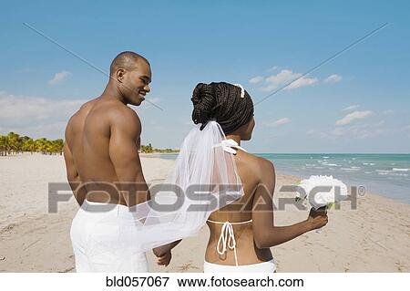 Stock Photo - African bride and groom holding hands at beach. Fotosearch