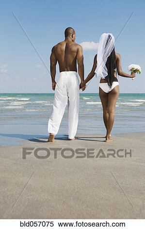 Stock Photography - African bride and groom holding hands at beach. Fotosearch