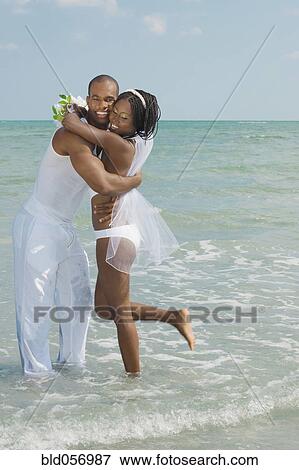 Stock Photo - African bride and groom hugging at beach. Fotosearch