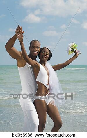 Stock Photograph - African bride and groom hugging at beach. Fotosearch