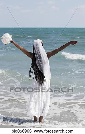 Stock Image - African bride standing in ocean surf. Fotosearch