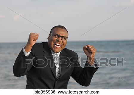Stock Photograph - African businessman cheering in front of water. Fotosearch