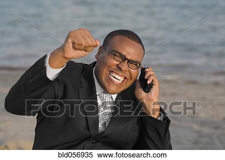 Stock Photography - African businessman cheering on cell phone. Fotosearch
