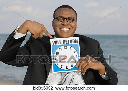 Stock Image - African businessman holding clock sign. Fotosearch