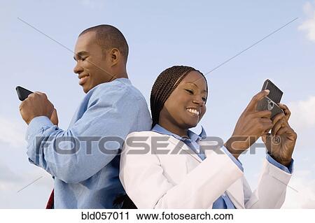 Stock Image - African businesspeople looking at cell phones. Fotosearch
