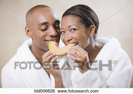 Stock Photograph - African couple in bathrobes eating melon. Fotosearch