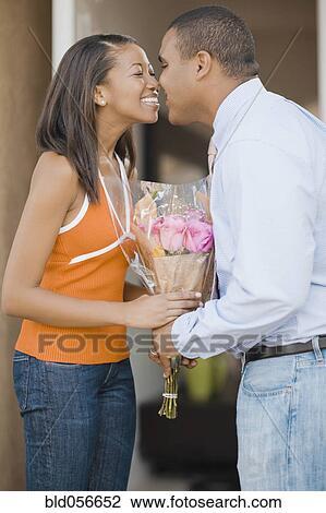 Stock Image - African couple rubbing noses over bouquet of flowers. Fotosearch