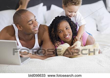 Stock Image - African family laying on bed. Fotosearch