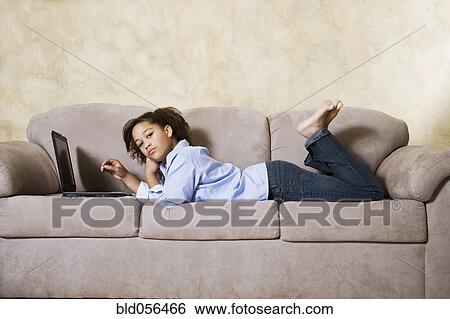 Stock Photograph - African girl with laptop on sofa. Fotosearch