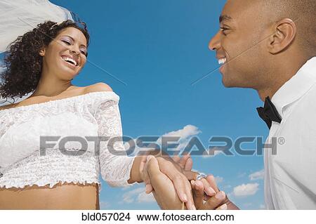 Picture - African groom putting ring on bride’s finger. Fotosearch