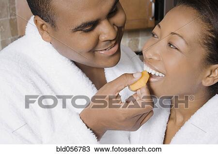 Stock Image - African man feeding fruit to wife. Fotosearch