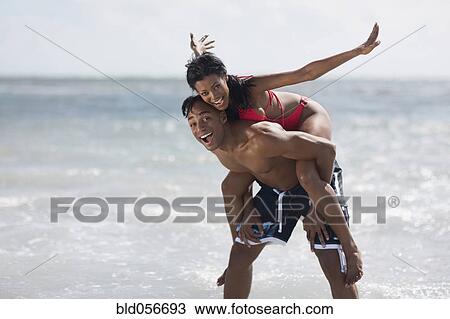 Stock Image - African man giving girlfriend piggy back ride. Fotosearch