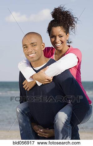 Stock Photo - African man giving girlfriend piggy back ride. Fotosearch