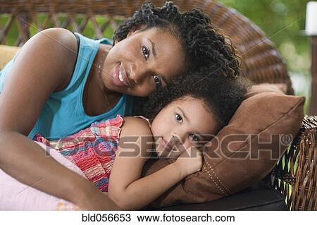 Stock Image - African mother and daughter laying on sofa. Fotosearch