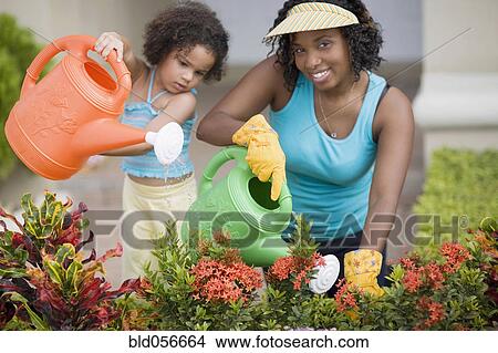 Picture - African mother and daughter watering flowers. Fotosearch