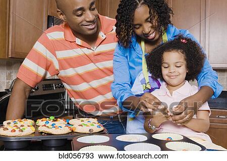 Stock Image - African parents and daughter making cupcakes. Fotosearch