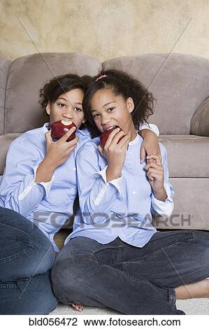 Stock Image - African twin sisters eating apples. Fotosearch