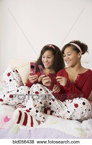 Stock Photo - African twin sisters looking at cell phones. Fotosearch