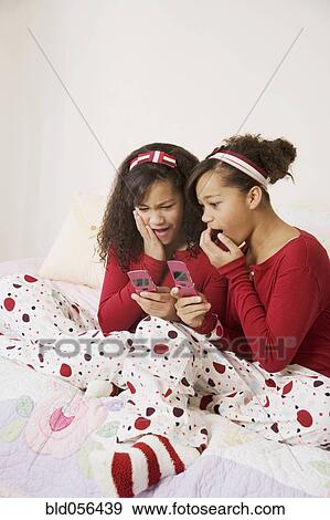 Stock Photo - African twin sisters looking at cell phones. Fotosearch