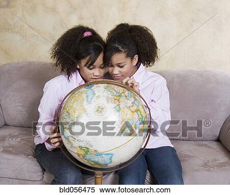 Stock Photography - African twin sisters looking at globe. Fotosearch