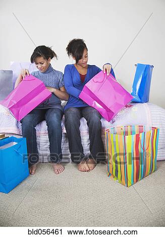 Stock Image - African twin sisters looking in shopping bags. Fotosearch