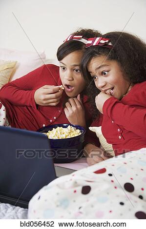 Stock Image - African twin sisters watching movie. Fotosearch