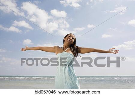 Stock Photograph - African woman with arms outstretched at beach. Fotosearch